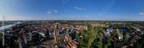 Super wide 180 degree cityscape aerial panorama of the Dutch medieval Hanseatic city with Walburgiskerk cathedral tower lit up in sunlight in urban landscape.