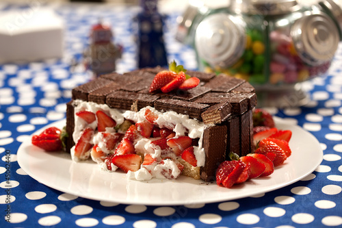 Torta de biscoito de chocolate recheada de creme e pedaços de morango em prato branco e mesa decorada.