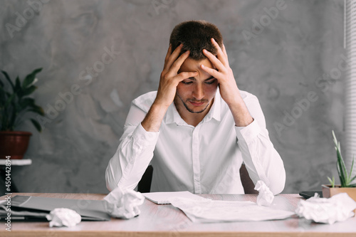 Portrait of businessman man with headache sitting in company office. Solving financial problems. Creative crisis and depression. Professional burnout of an employee without inspiration.