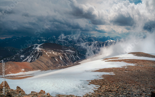 Snow storm on the top of a mountain. Wonderful dramatic landscape with big snowy mountain peaks above low clouds. Atmospheric large snow mountain tops in cloudy sky.