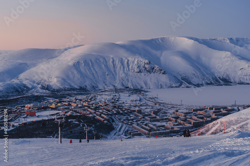 Polar city on the shore of a frozen lake surrounded by snow-capped mountains at dusk in Russia, Murmansk region, Kirovsk. Winter holiday in Arctic, Khibiny Mountains. 