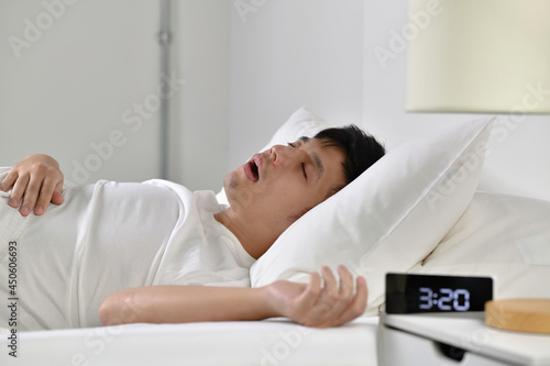 Young Asian man sleeping and snoring loudly lying in the bed.