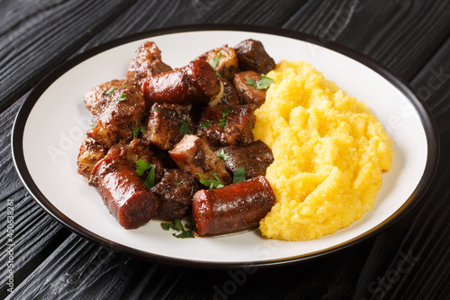 Romanian food pomana porcului made from chunks of fried pork, sausages and offal served with corn porridge close-up in a plate on the table. horizontal