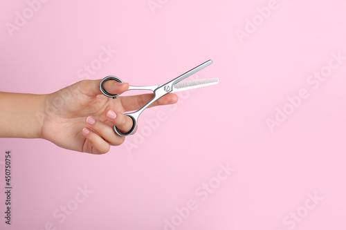Hairdresser holding professional thinning scissors and space for text on pink background, closeup. Haircut tool