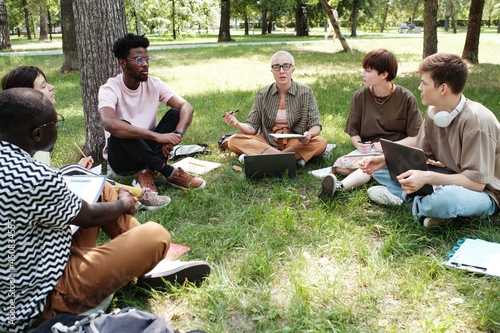 Group of students sitting on the grass and listening to their teacher they studying in the park outdoors