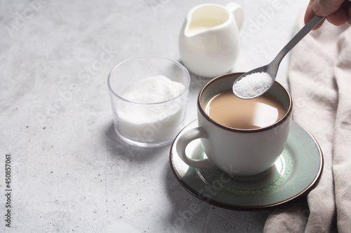 Spoon with sweetener over a cup of milk coffee