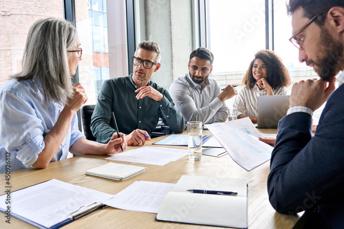 Diverse international executive business partners group discuss report at boardroom meeting table. Multiracial team negotiating project developing business strategy doing paperwork analysis in office.