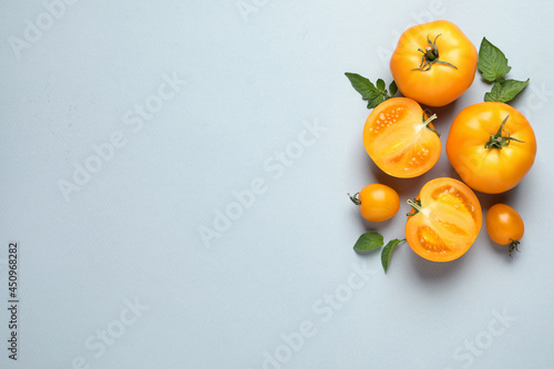 Cut and whole ripe yellow tomatoes with leaves on light background, flat lay. Space for text
