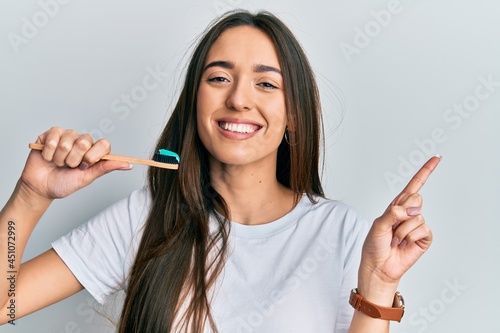 Young hispanic girl holding toothbrush with toothpaste smiling happy pointing with hand and finger to the side