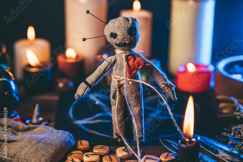 Voodoo doll studded with needles in magical table with candles and occult objects. Magic and dark spooky ritual. Retribution or revenge through witchcraft concept.
