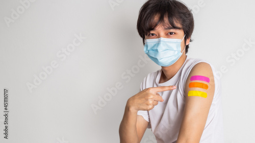 Asian man wearing face mask with a smile on his face showing his vaccinated arm. fight against virus covid-19 coronavirus, Vaccination and immunization. vaccine booster concept.