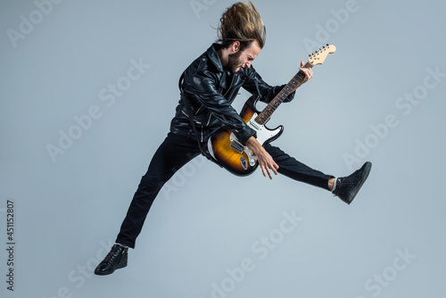 emotional bearded rock musician playing electric guitar in leather jacket and jumping, guitar player