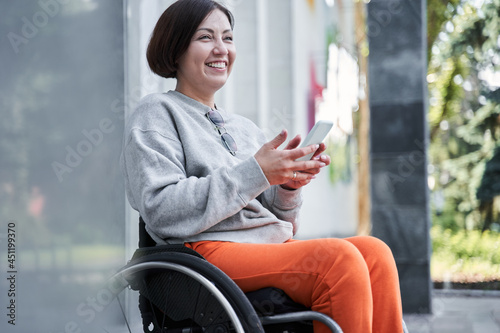 Disabled woman holding smartphone and looking away while sitting at the wheelchair