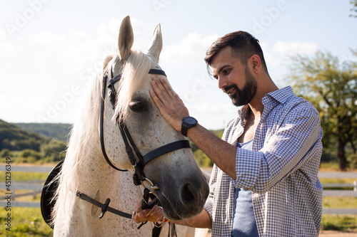 The happy man is stroking a white horse in a ranch