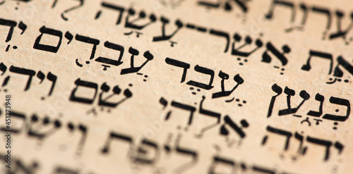 Closeup of hebrew words in Torah page that translate in english as Cursed be Canaan, a servant of servants shall he be to his brothers. Selective focus. Banner.