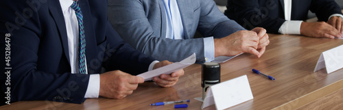 Hands of businessmen, politicians or lawyers on the table next to the document and the stamp. Meeting, analysis and signing of documents. Reflections on benefits. Selective focusing