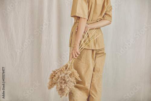 Young girl model in a pantsuit with her back on a linen background with spikelets in her hands close-up