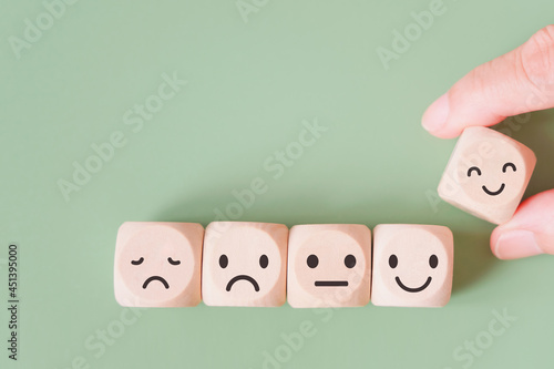 hand selected happy face wood cube and others on green background for customer service evaluation, feedback, satisfaction survey or mental heath concept