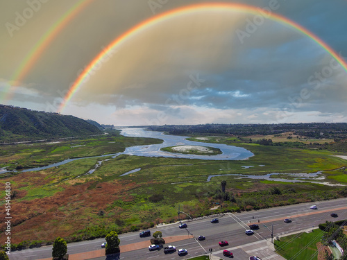 a gorgeous aerial shot of the blue lagoon waters surrounded by lush green trees and plants with blue sky, powerful clouds and a rainbow at Batiquitos Lagoon in Carlsbad California USA