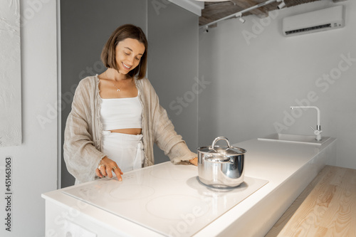 Young stylish woman cooking on induction hob at modern kitchen. Concept of smart technologies of kitchen appliances
