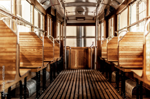 Wnętrze zabytkowego tramwaju z drewnianymi ławkami i klasycznym, eleganckim wykończeniem. Symetryczny układ siedzeń i widok na tylną część pojazdu dodają głębi i podkreślają nostalgiczną atmosferę.