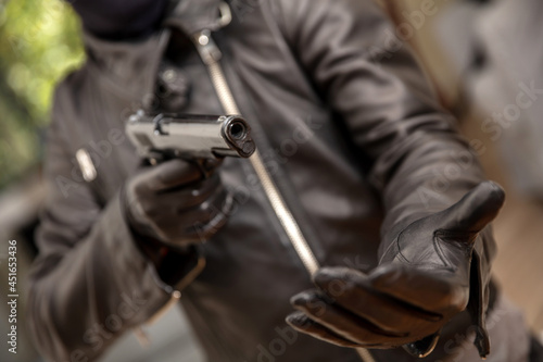 Thief gloved hand holding a pistol aiming, closeup view. Armed robbery concept