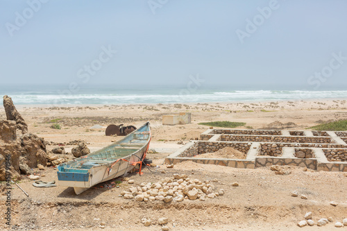 small fishery boat and remaining foundation of the stone house beside the beach of arabian sea in mahrah region, yemen