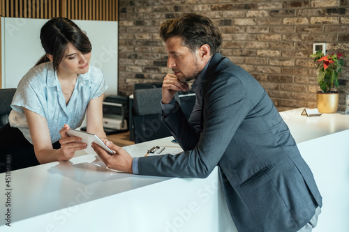 Businessman Using Digital Tablet for Checking In at Hotel.Smiling female concierge standing at hotel reception and showing available rooms on digital tablet to the new guest.