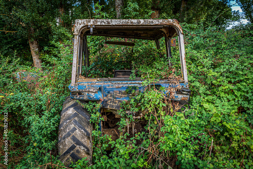 Old abandoned rusty tractor covered by bramble