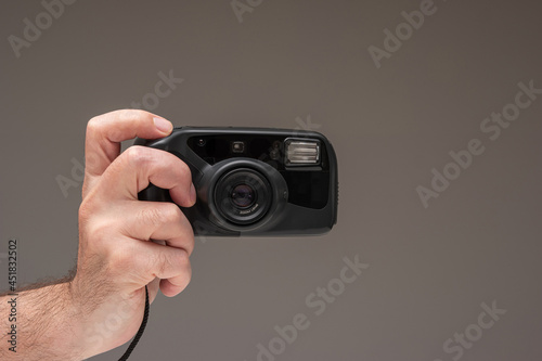Caucasian male hand holding a generic old film point and shoot camera. Close up studio shot, isolated on brown background
