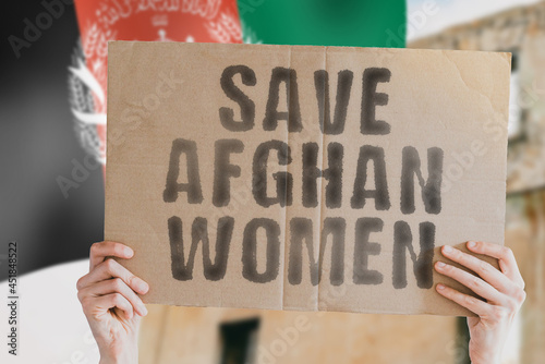 The phrase " Save afghan women " on a banner in men's hand with blurred Afghan flag on the background. Protest. Riot. Violence. Collapse. Politics. Streets. Save. Cruelty. Religion. Help. Afghanistan