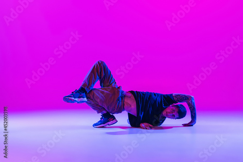 Modern dance style. Hip hop, break dancing dancer in action, motion in dark clothes isolated over bright magenta background at dance hall in neon light.