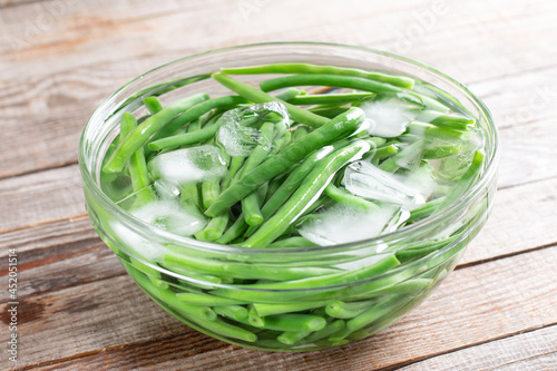 Green beans in a colander. Boiled or blanched vegetables in ice water on a table