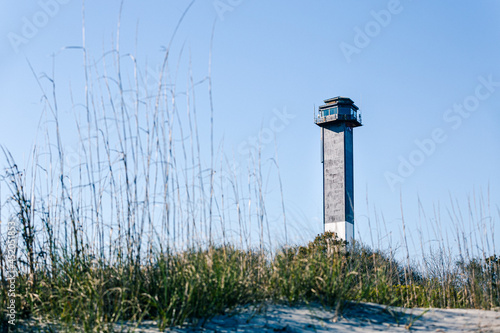 Sullivan's Island Lighthouse. Clear daytime weather. Beach dunes and grass in foreground.