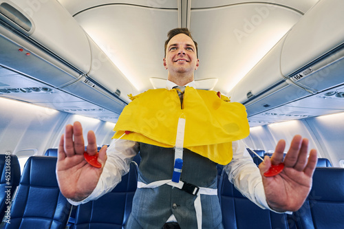 Smiling young steward inflating his the lifejacket aboard the aircraft