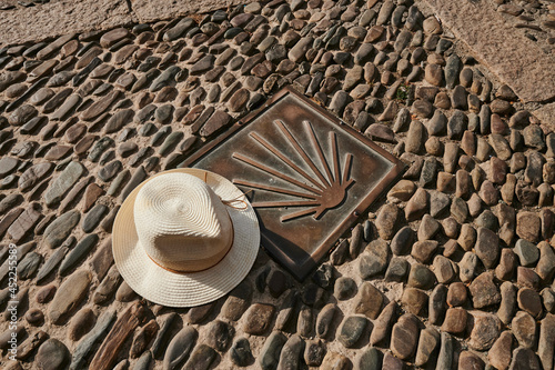 hat next to the symbol of the Camino de Santiago on a cobbled street