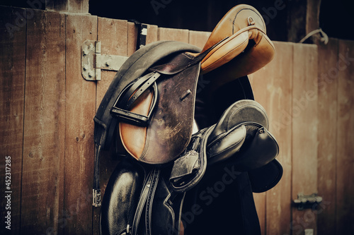 Brown and black saddles hang on the stall. Horse ammunition.