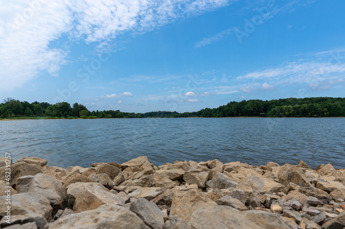 Gorgeous sunny summer day at Freeman Lake in Elizabethtown, KY. Composed with rocks in the foreground and a blue sky with some clouds in the sky.