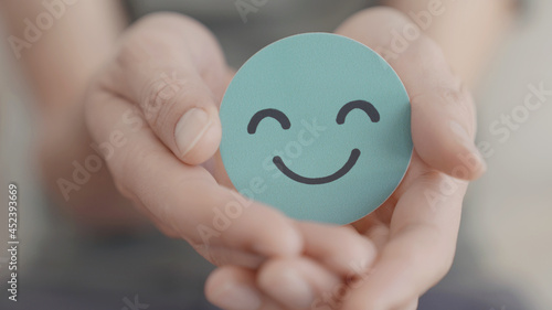 Hand holding green happy smile face paper cut, mental health assessment, child positive wellness, world mental health day, compliment day, mindful concept