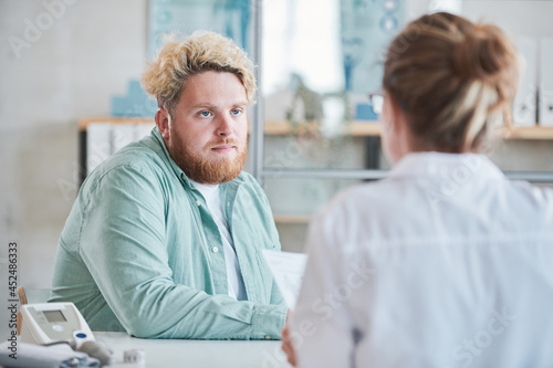 Young overweight man sitting at the table at hospital he visiting a doctor for having a nutrition recommendations