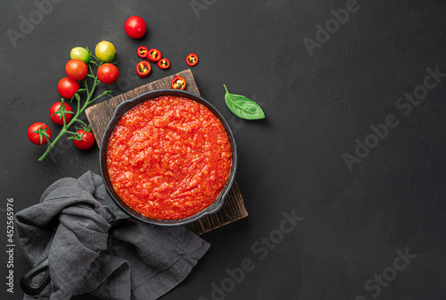 Tomato sauce in a frying pan on a wooden board on a black background. Marinara sauce with basil. Top view, copy space.