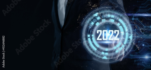 Smart businessman pointing digital dashboard in 2022 on dark blue background. Futuristic technology trend concept. Artificial intelligence (AI), machine learning support for enhancing business growth.