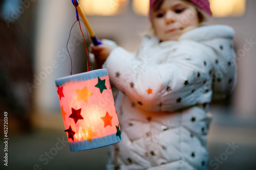 Close-up of little kid girl holding selfmade lanterns with candle for St. Martin procession. Healthy toddler child happy about children and family parade in kindergarten. German tradition Martinsumzug
