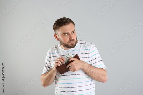 Greedy young man hiding wallet with money on light grey background