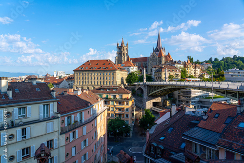 View of the beautiful city of Lausanne in Switzerland in the morning, the cityscape is dominated by the Notre-Dame cathedral and the Bessières bridge and Rue Central, blue sky and sunshine 