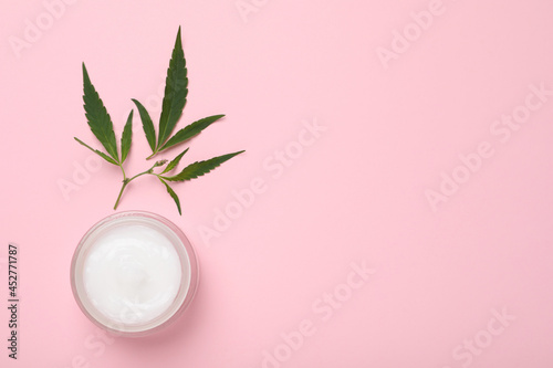 Glass jar of hemp cream on pink background, flat lay with space for text. Natural cosmetics