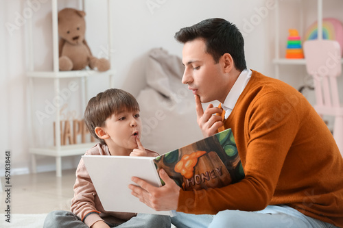 Speech therapist with little boy reading book in office