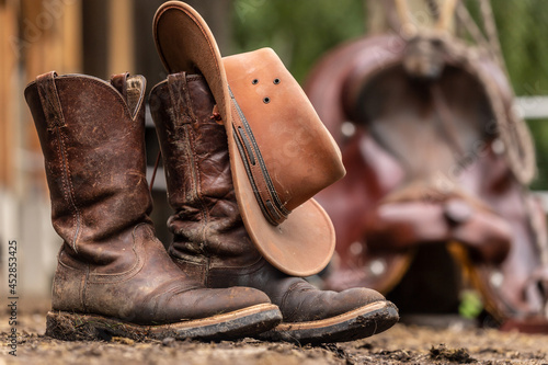Ranch life scenery: muddy western boots in front of a western saddle. Cowboy boots. Muddy working boots