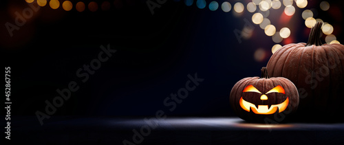 Two halloween lanterns with evil eyes and face on a wood table with a spooky dark blue background at night with light bokeh.