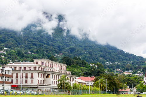 Victoria, Seychelles, 04.05.2021. Victoria town landscape view with colonial style office buildings on Independence Avenue seen from Freedom Square Grounds with cloudy mountains in the background.